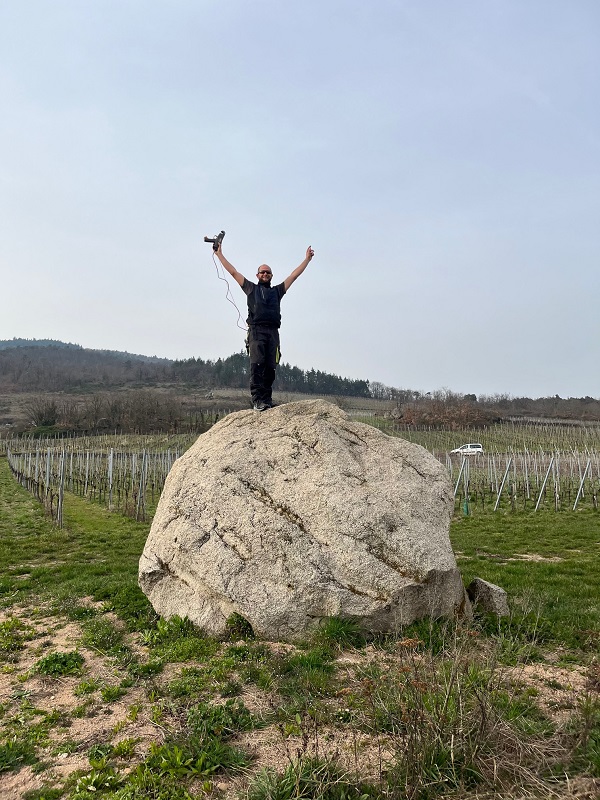 Gauthier standing on a rock celebrating the end of vine arcing, surrounded by vineyards in Dambach‑la‑Ville.