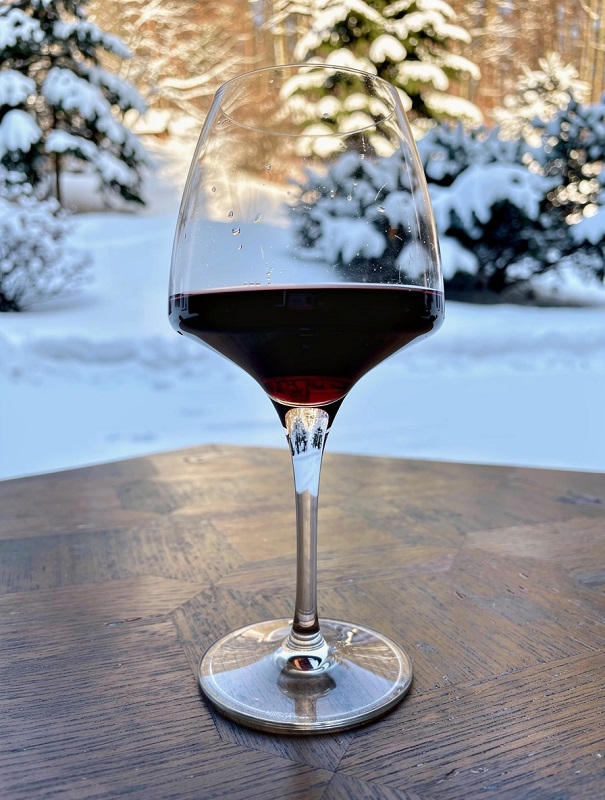 Glass of Alsace Pinot Noir red wine placed in the snow, humorously illustrating the mistake of serving wine too cold. Alsace wine temperature guide.