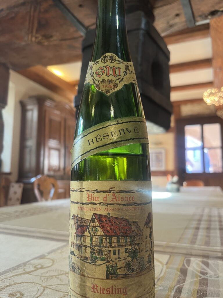 Bouteille de vin Riesling 1986 entamée, posée sous le pressoir historique en bois au caveau Schaeffer-Woerly.