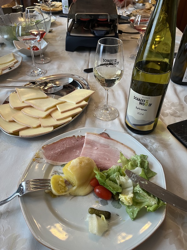Bouteille de Sylvaner 2024 du Domaine Schaeffer-Woerly avec une assiette de raclette, fromage fondu et charcuterie.